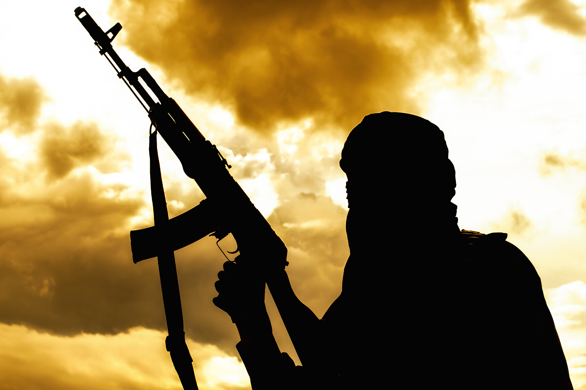 Muslim militant with rifle in the desert on sunset uder heavy clouds